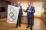 Dwóch mężczyzn w pokoju trzyma flagę olimpijską