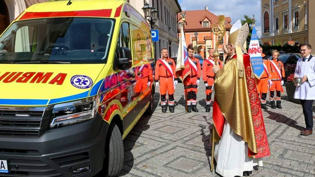 Biskup święci ambulans. Obok stoją ratownicy medyczni.