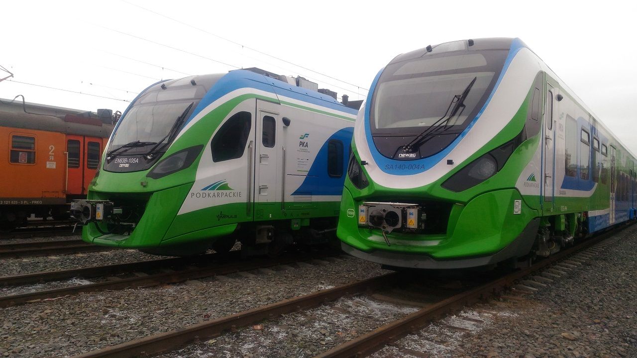 Na zdjęciu dwa pojazdy kolejowe – elektryczny po lewej i spalinowy po prawej - w barwach województwa podkarpackiego. Oba odstawione na bocznicy. 